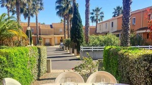 A patio with a table set for four, surrounded by white plastic chairs, overlooking a street with palm trees and buildings.