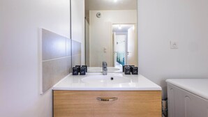 Un baño moderno con un lavabo blanco, un espejo grande y un armario de madera.