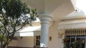 A patio area with a white column, a small tree, and a table with chairs.