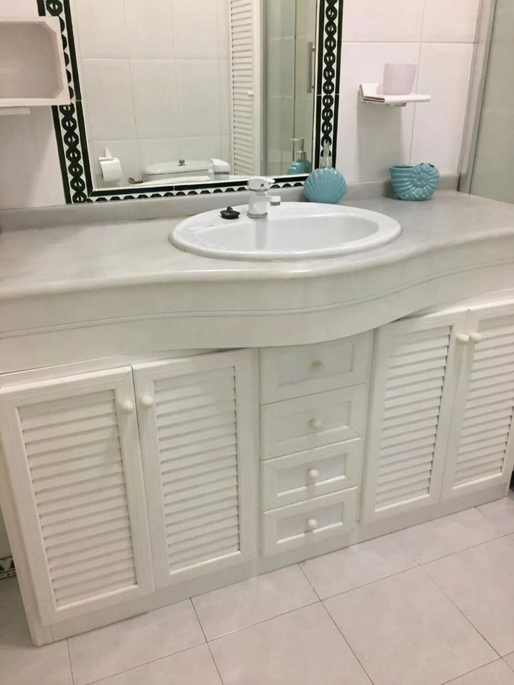 A bathroom with a white vanity, a round sink, and a mirror with a decorative frame.