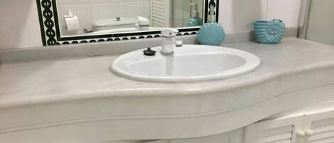 A bathroom with a white vanity, a round sink, and a mirror with a decorative frame.
