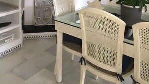 A dining area with a glass table and wicker chairs, a shelf with decorative plates, and a potted plant.