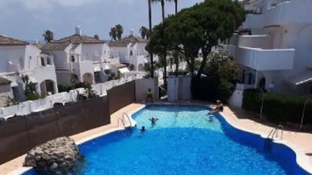 A swimming pool with clear blue water, surrounded by white buildings and greenery.