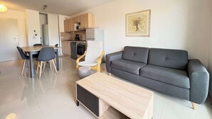 Una sala moderna con un sofá gris, una mesa de centro de madera, una mesa de comedor con sillas y una zona de cocina con armarios y electrodomésticos de madera.