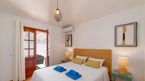 A bedroom with a wooden headboard, a white quilted bedspread, two blue towels, a green nightstand with a lamp, and a wicker basket. - Villa Family by Villa Plus (Puerto del Carmen)