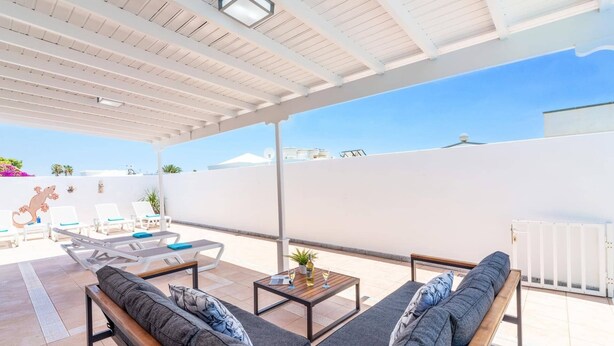 A covered outdoor seating area with lounge chairs and a sofa, a table with drinks, and a view of the sky and buildings. - Villa Family by Villa Plus (Puerto del Carmen)