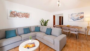 A modern living room with a grey sectional sofa, a round coffee table, and a dining area with a wooden table and chairs. - Villa Family by Villa Plus (Puerto del Carmen)