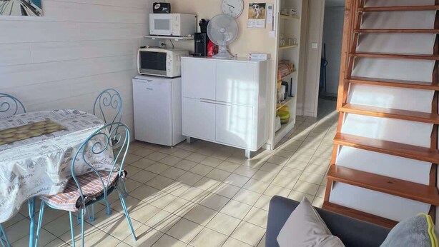 Un espacio habitable compacto con kitchenette, una zona de comedor con mesa y sillas, un sofá y una escalera.