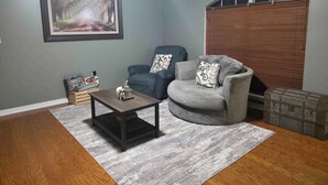 A living room with a dark wooden coffee table, two grey armchairs, a framed picture on the wall, and a wooden chest of drawers. - Northgate Home (Bossier City)