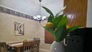 A dining area with a table and chairs, a vase with flowers, a painting on the wall, and a ceiling light. - Northgate Home (Bossier City)