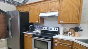 A kitchen with wooden cabinets, a stainless steel refrigerator, a coffee maker, and a stove. - Northgate Home (Bossier City)