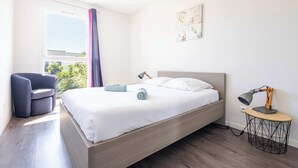 Une chambre moderne avec un lit, un bureau doté d’une lampe, une chaise et une fenêtre avec des rideaux.