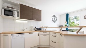 Une cuisine moderne avec des meubles blancs, un lave-vaisselle, un four à micro-ondes et une horloge au mur.