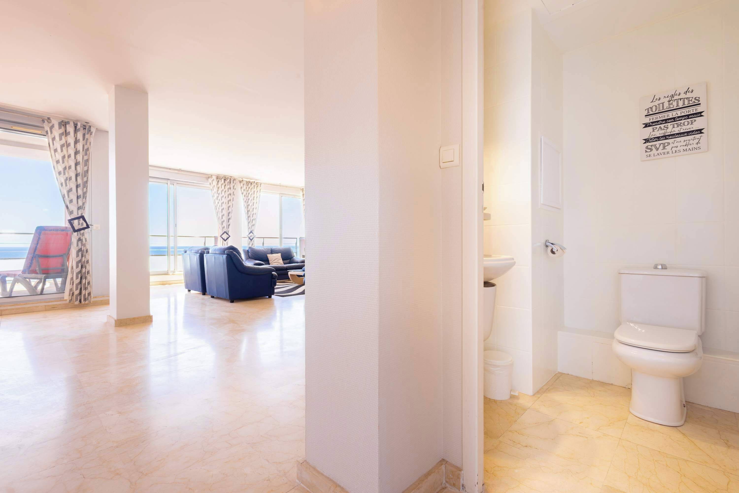 A hotel room with a balcony, a sofa, a coffee table, and a bathroom with a toilet and sink.