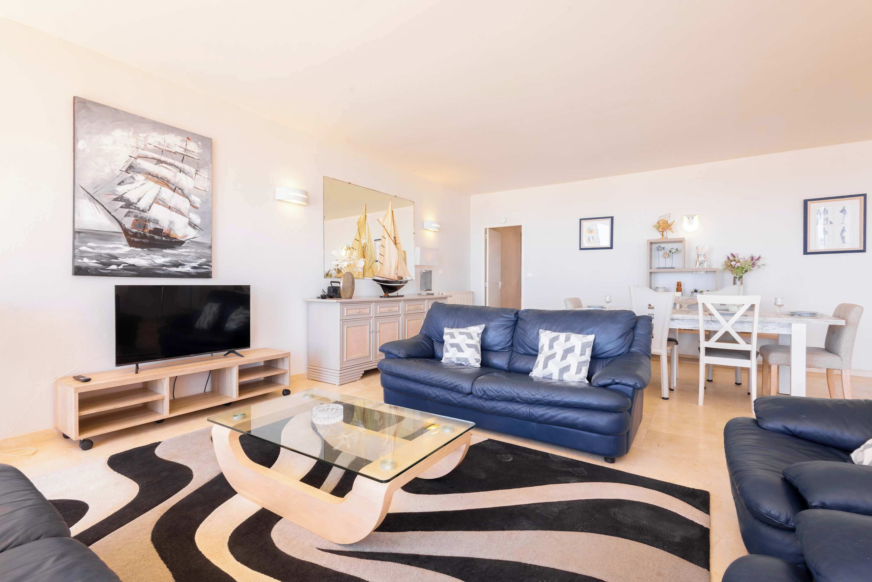 A modern living room with a sofa, a glass coffee table, a flat-screen TV, and a dining area with a table and chairs.