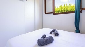 A hotel room with a bed, a TV mounted on the wall, a window with a view of greenery, and a curtain.