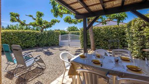 An outdoor patio with a table set for dining, surrounded by chairs, and a pergola overhead.
