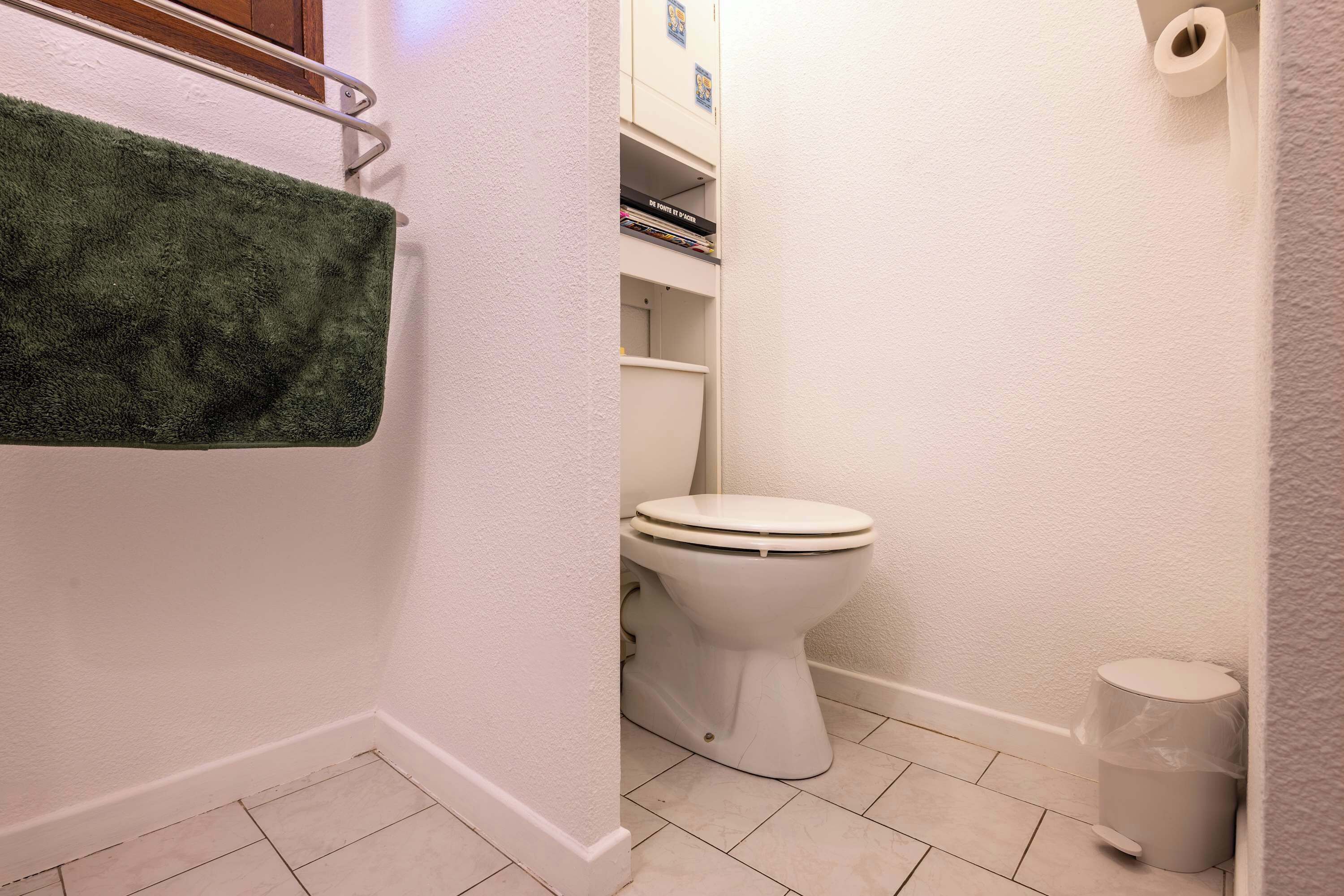 Une salle de bain équipée de toilettes, d’une poubelle et d’un porte-serviettes sur lequel est posée une serviette verte.