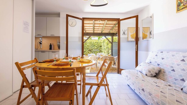 A dining area with a wooden table and chairs, a sofa with patterned cushions, and a view of an outdoor patio.