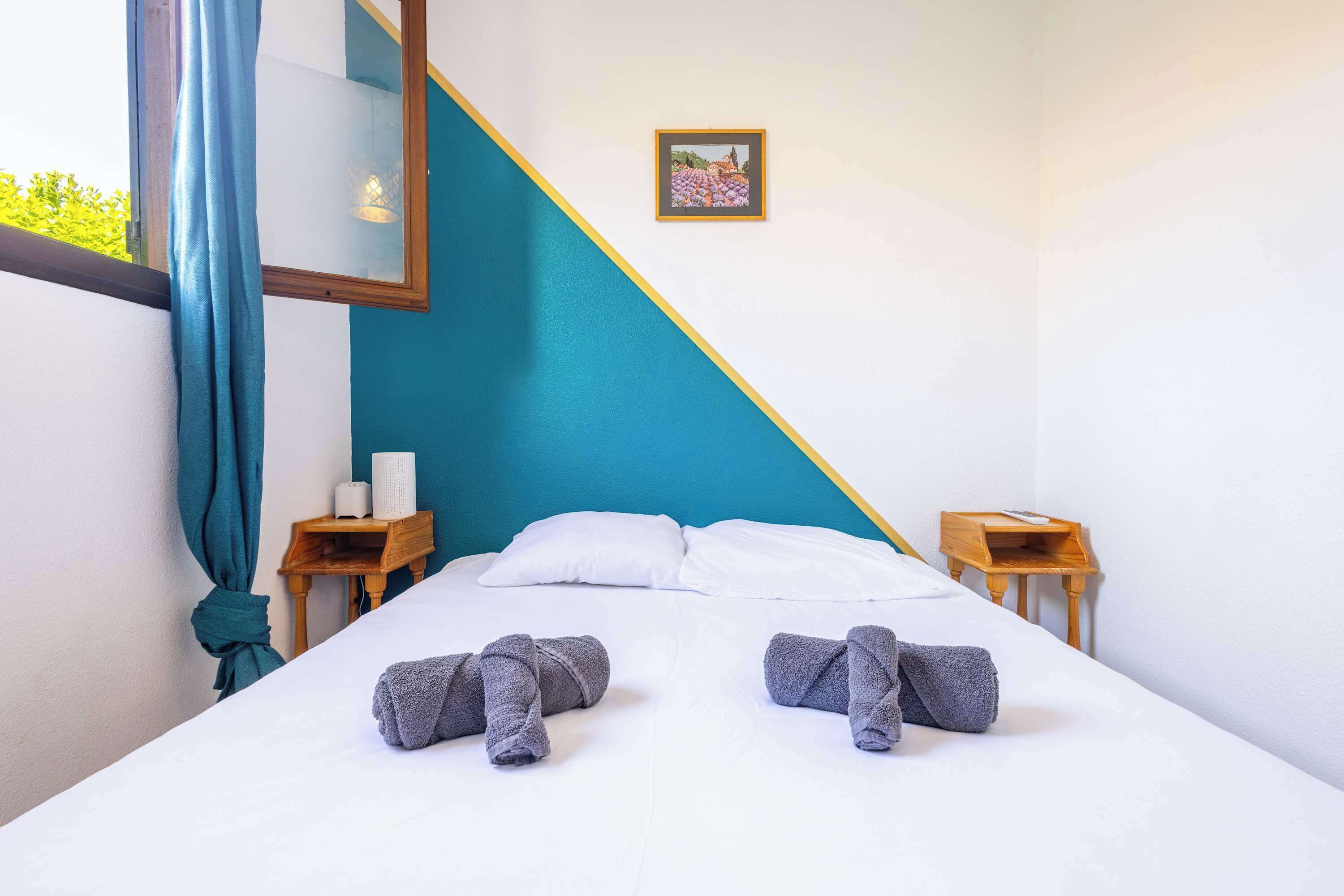 A neatly made bed with two towels, a bedside table with a lamp, and a picture on the wall.