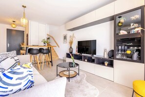 Un salon moderne comprenant un canapé, une table basse, un téléviseur et un coin repas avec des chaises et une table.