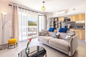 A modern living room with a sofa, a glass coffee table, and a yellow ottoman. - Les terrasses étoilées (Sérignan)