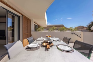 Un espace repas avec une table dressée pour six personnes, des sièges à l’extérieur et une vue sur les maisons voisines.