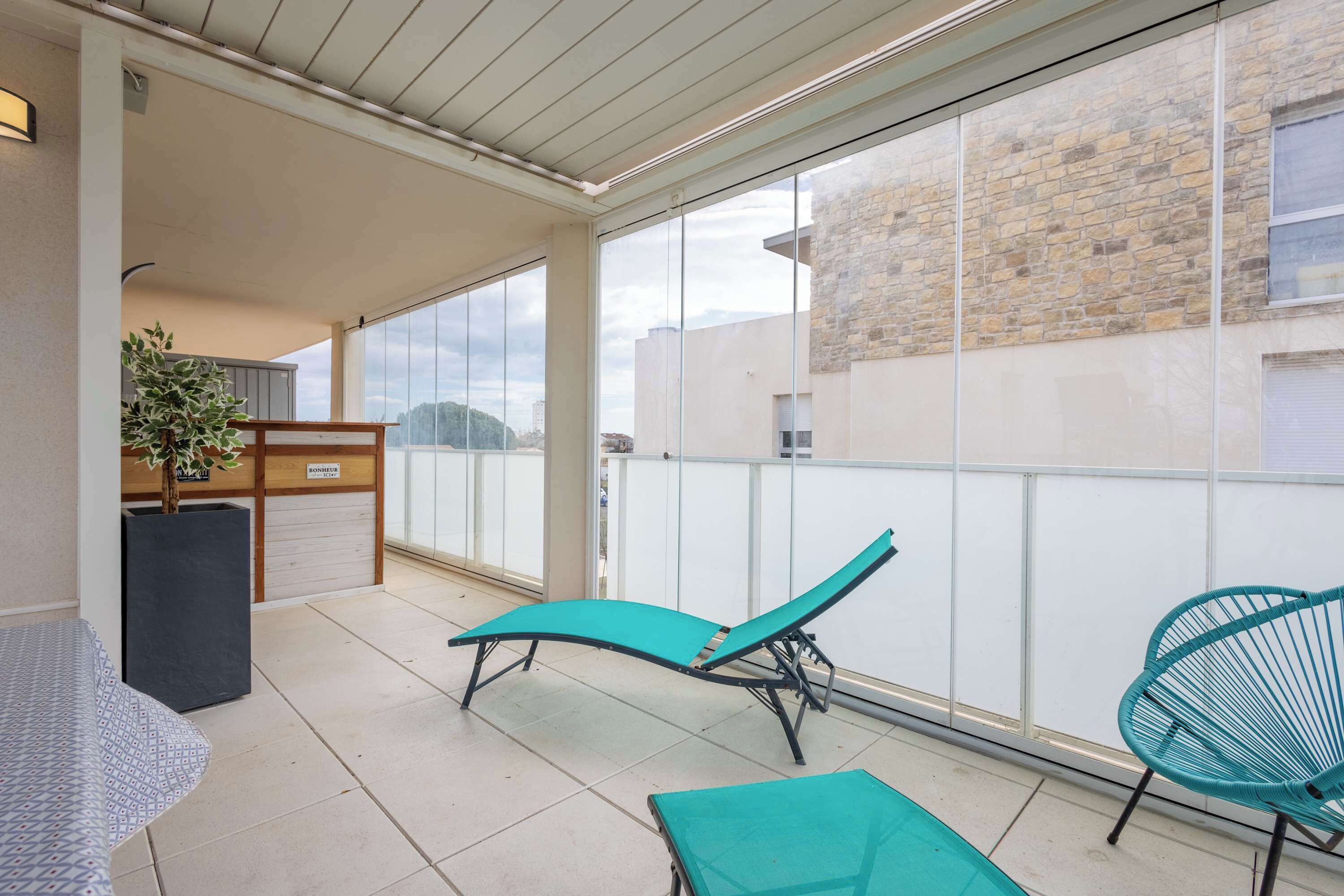 A balcony with a sun lounger, a chair, and a potted plant.