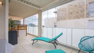 A balcony with a sun lounger, a chair, and a potted plant.