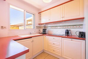 Una cucina con mobili bianchi, un piano di lavoro rosso, una finestra e uno schienale piastrellato.