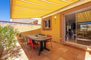 Un patio esterno con tavolo e sedie, un tendone giallo e vista verso l'interno della casa.