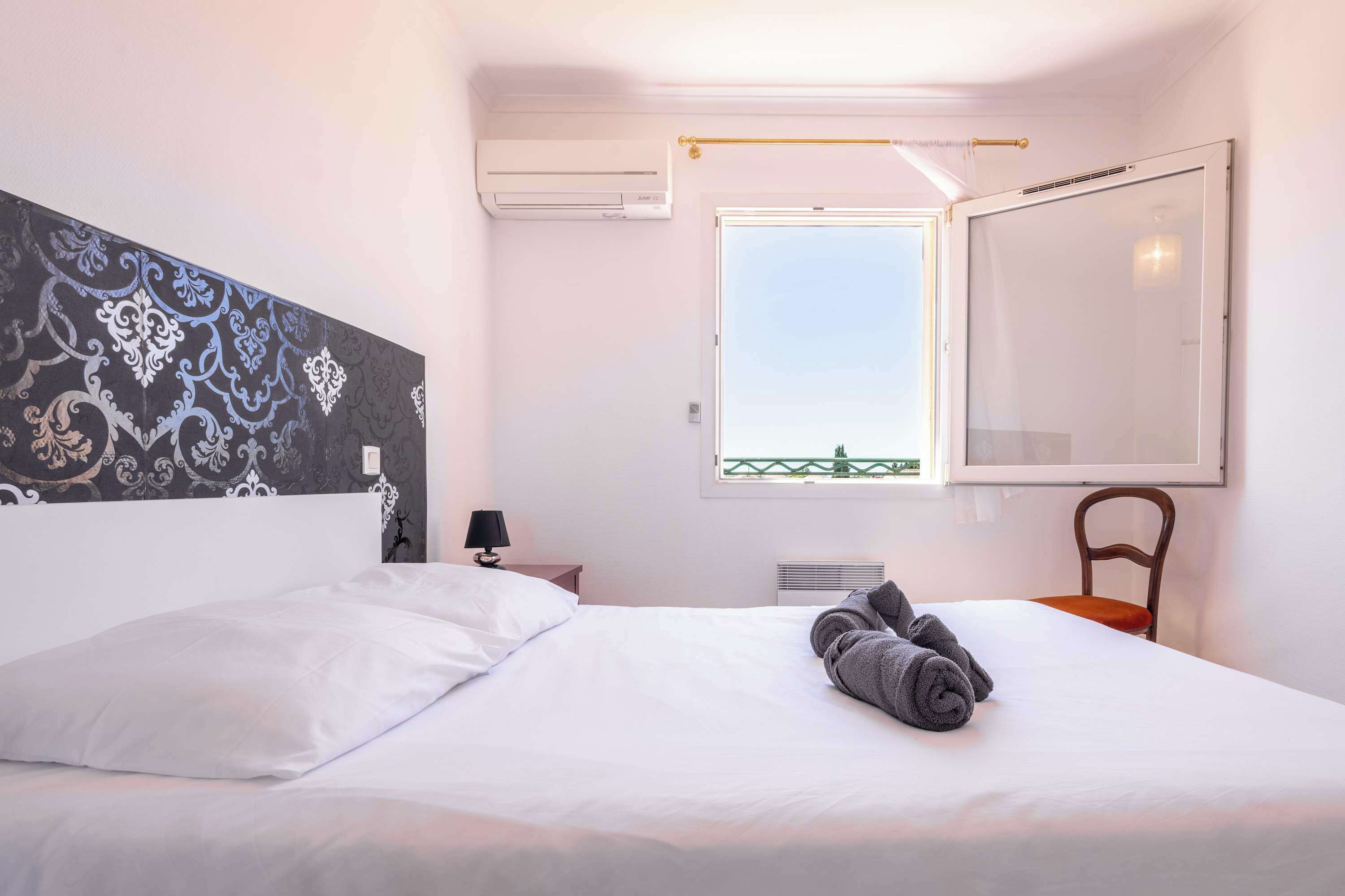 Ein Hotelzimmer mit Bett, Fenster mit Blick, Wand-Klimaanlage und einem Sessel.