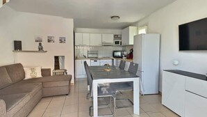 Ein modernes Wohnzimmer mit einer Couch, einem Esstisch mit Stühlen, einer Küchenzeile mit Schränken und Geräten sowie einem an der Wand befestigten Fernseher.