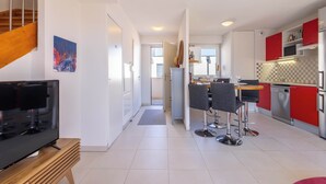 A modern kitchen with red cabinets, a dining area with bar stools, a TV on a wooden stand, and a staircase. - Villa Bianca – Spacious Apartment (Sérignan)