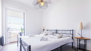 A modern bedroom with a metal bed frame, white bedding, a potted plant, and a view through a glass door. - Valras 'Loc Archipel Panarea - Cap Horizon (Valras-Plage)