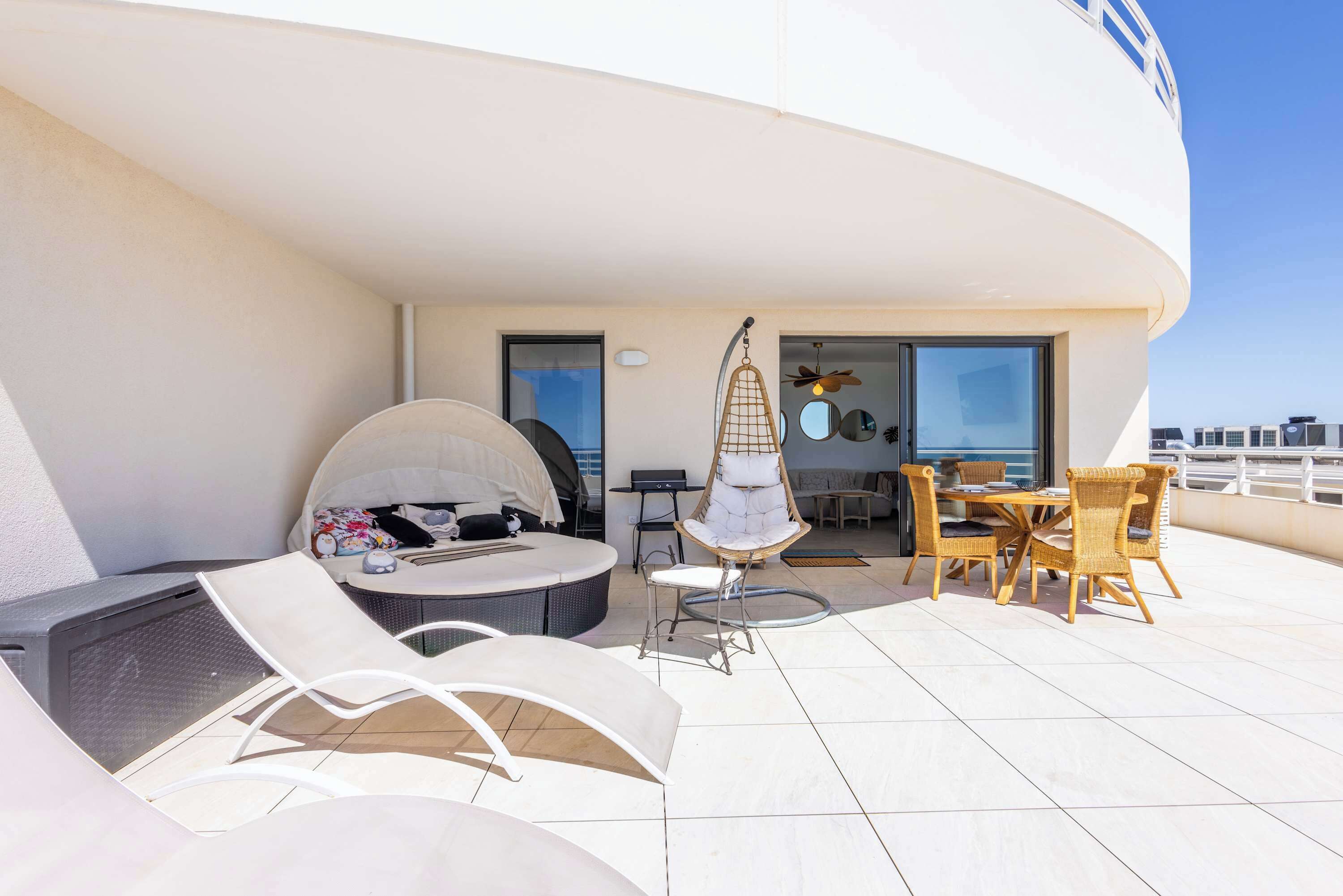 Une terrasse sur le toit, aménagée avec des chaises longues, une table à manger et un fauteuil suspendu.