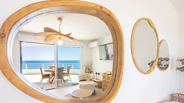 A room with a large mirror, a ceiling fan, a dining area with a table and chairs, and a view of the ocean. - Valras 'Loc Archipel Panarea - Cap Horizon (Valras-Plage)