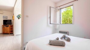 A bedroom with a bed, a window with a view of greenery, a television, and a wardrobe.
