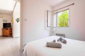 A bedroom with a bed, a window with a view of greenery, a television, and a wardrobe.