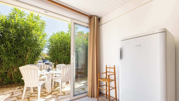 A room with a sliding glass door leading to an outdoor area, a white refrigerator, and a dining table with chairs.