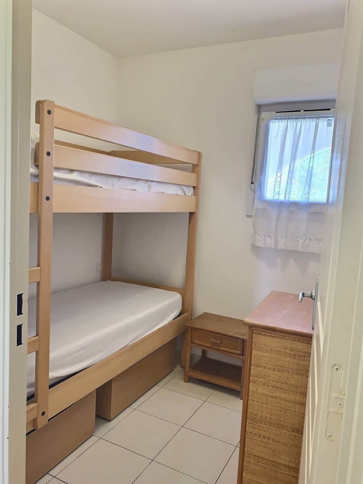Una cama litera con un escritorio pequeño y una ventana con cortinas.