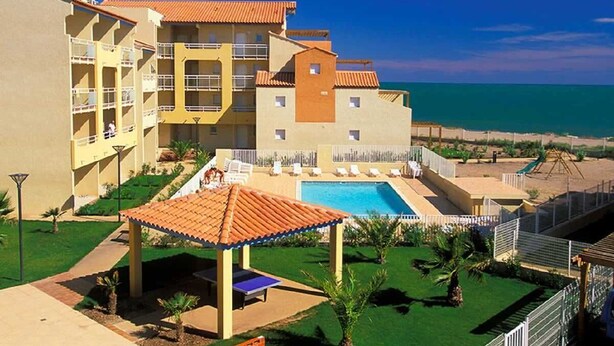 A hotel with a pool, beach view, and multiple balconies.