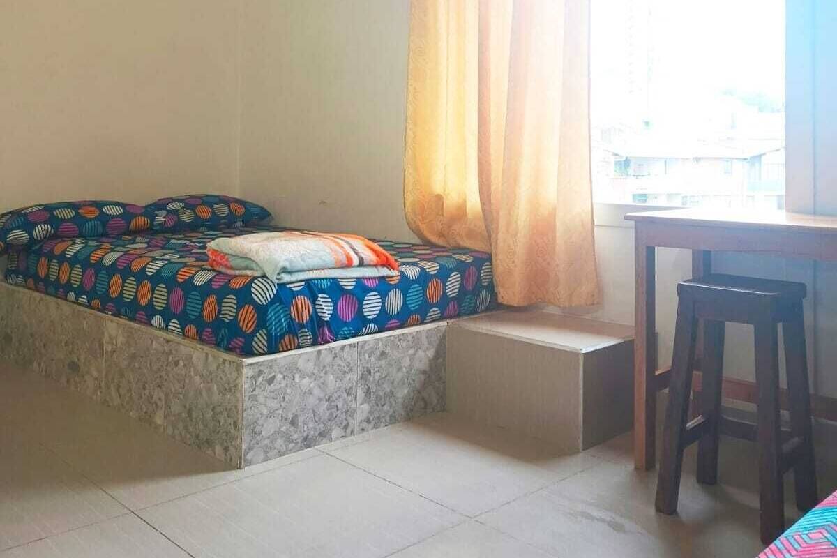 Une chambre avec un lit, un bureau et une fenêtre avec des rideaux.