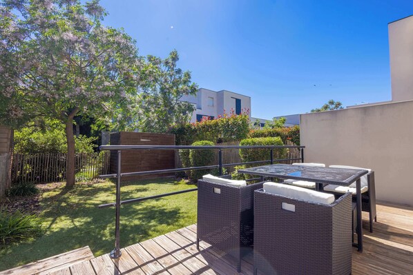 An outdoor patio with a table and chairs, surrounded by a wooden deck and a fenced garden area. - Villa Bianca – pavilion near Valras Beach (Sérignan)