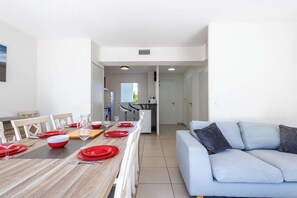 A modern living room with a light blue sofa and a dining area with a wooden table set for four. - Villa Bianca – pavilion near Valras Beach (Sérignan)