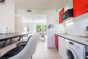 A kitchen with a washing machine, a microwave, and a dining area with chairs and a table. - Villa Bianca – pavilion near Valras Beach (Sérignan)