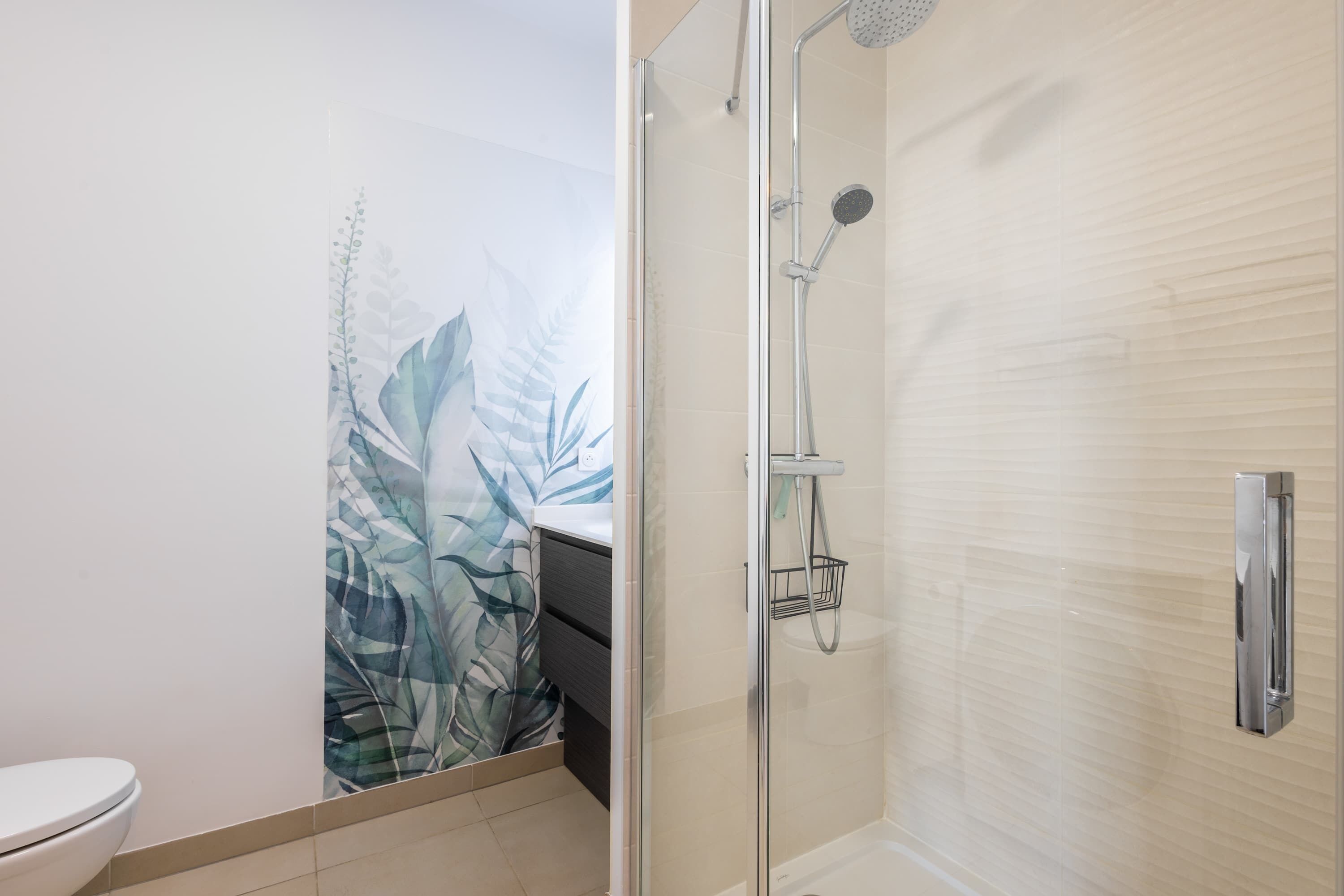 A bathroom with a toilet, a shower with a glass door, and a wall with a leaf pattern.