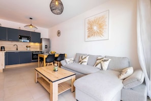 A modern living space with a kitchen, dining area, and a grey sofa with decorative pillows. - Valras'Loc Archipel Panarea Sea View and Comfort (Valras-Plage)