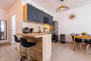 Et moderne køkken med en træø, sorte barstole, et spisebord med stole og en hængende lampe.
