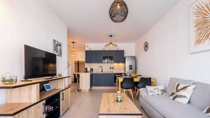 Una sala de estar moderna con un televisor de pantalla plana, muebles de madera, un sofá gris y una cocina al fondo.